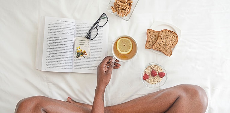 A girl sat on a bed with a book and healthy food 